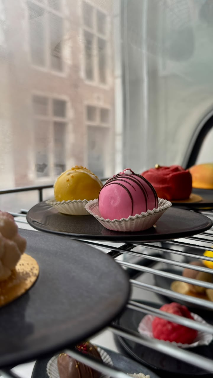 Glazed dome desserts in yellow, pink and red on dark plates by the café window