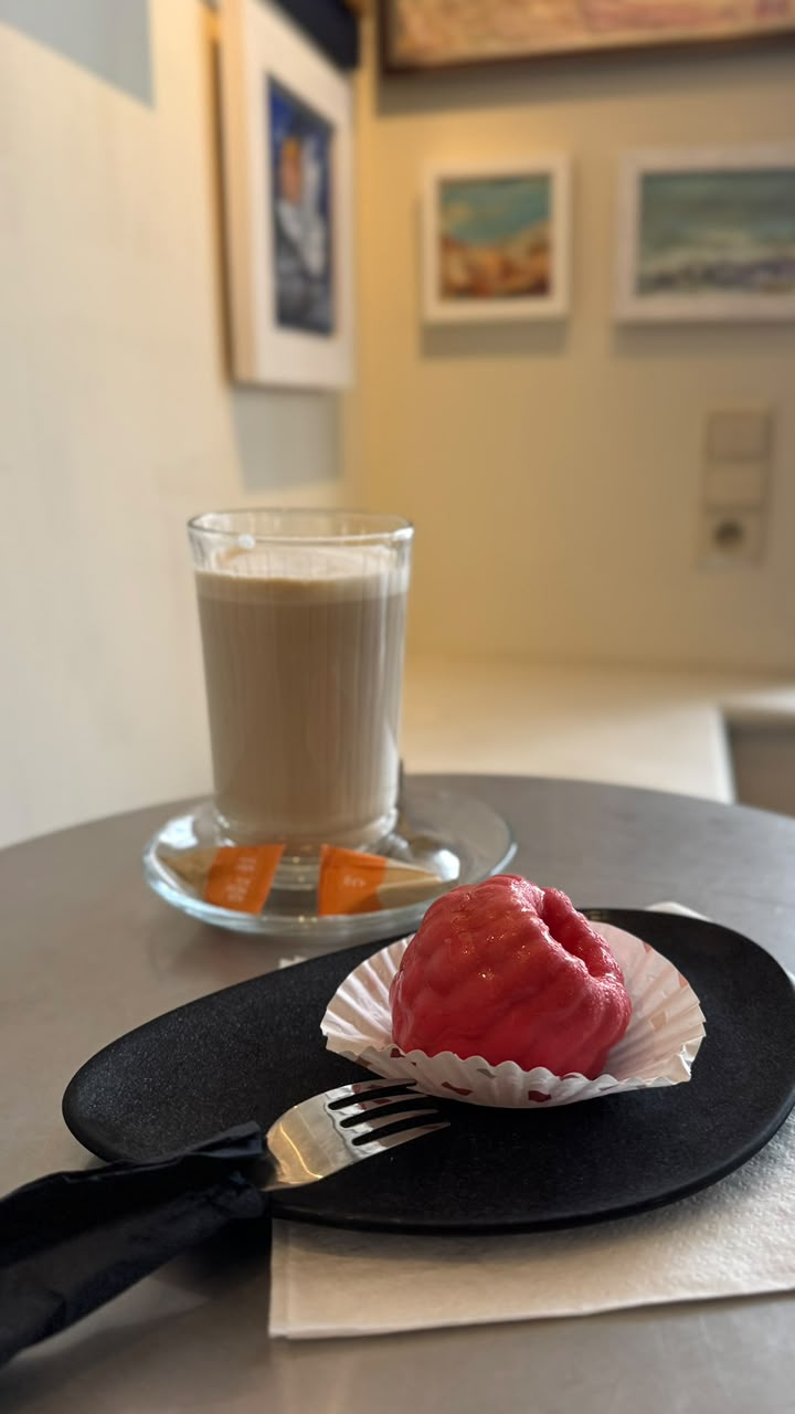 Latte in a tall glass next to a raspberry dessert on a black plate
