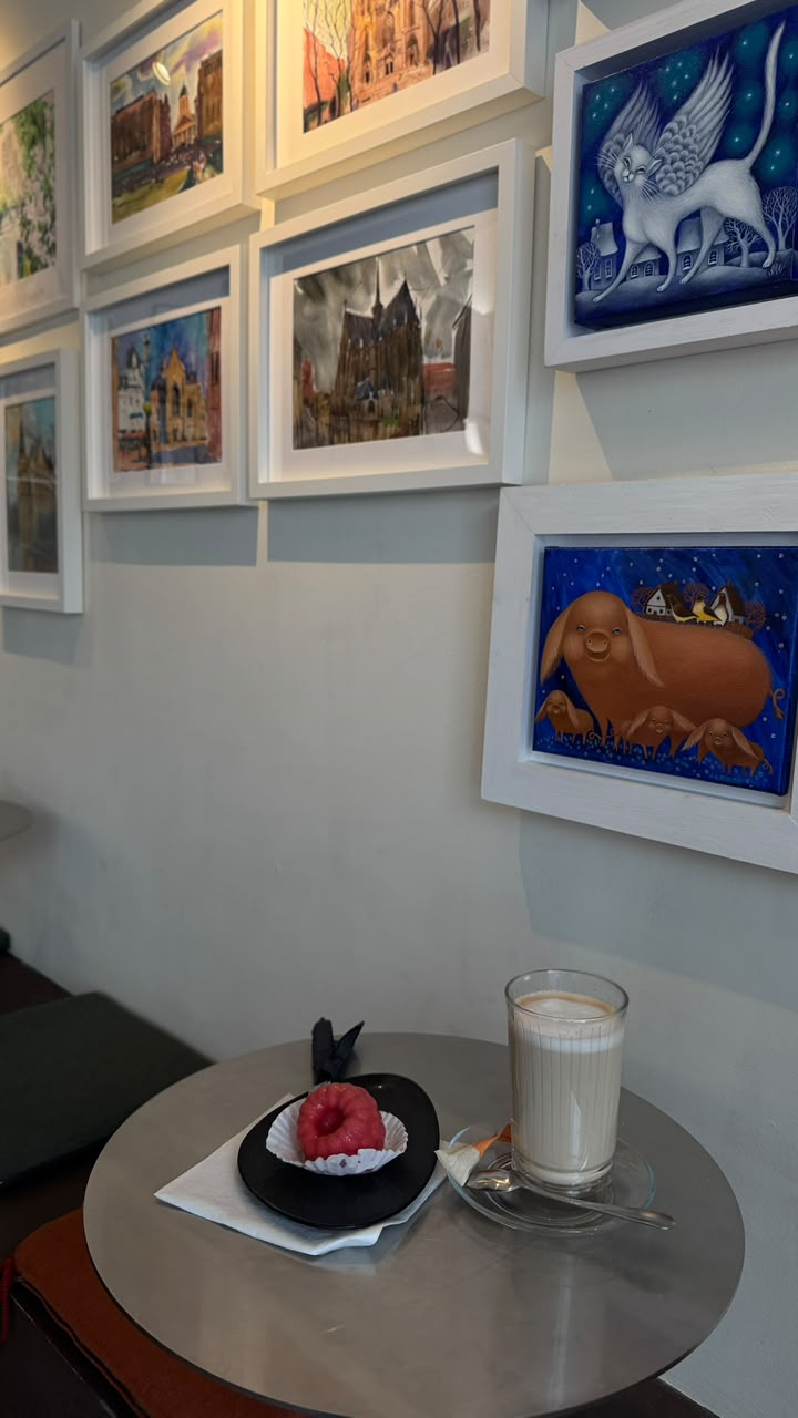 Latte and raspberry dessert on a small table beneath framed paintings of Brussels